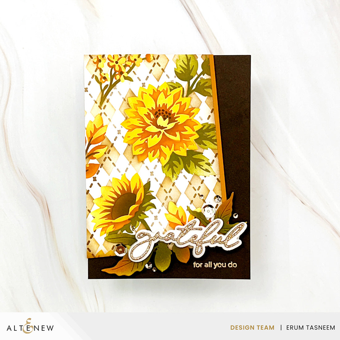 A handmade greeting card featuring a layered design with yellow and orange sunflowers, a white diamond-patterned background, a dark brown band, and a die-cut 'grateful for all you do' script element, displayed on a white marble surface.