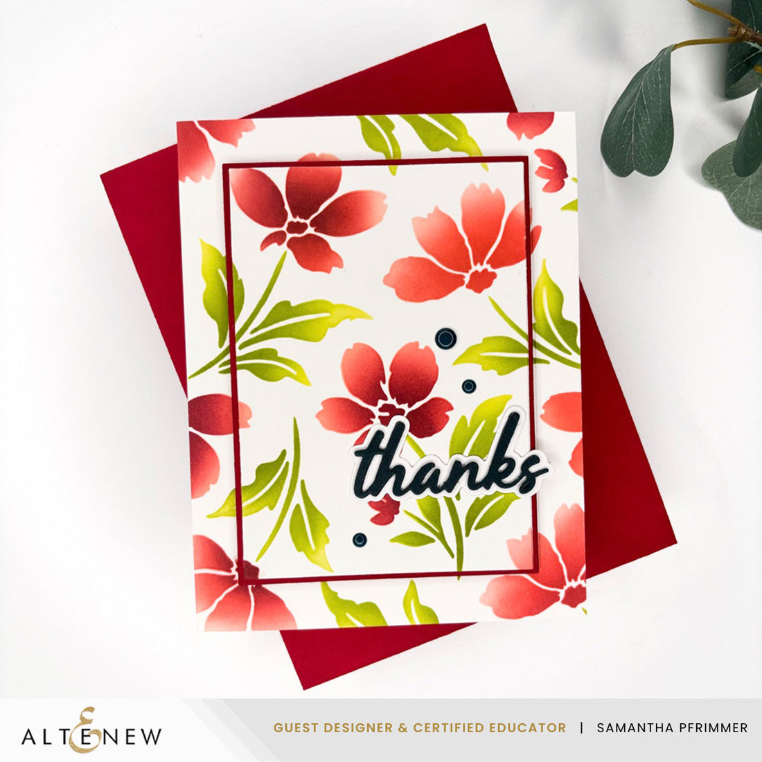 A handmade greeting card with a white background, red poppy flowers, green leaves, and the word 'thanks' in black script, layered over a dark red envelope. The card is photographed on a white surface with decorative green leaves in the corner. Altenew Painted Petals Stencil Set (3 in 1) card ideas