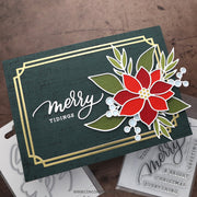 A handmade Christmas greeting card with a dark green textured background, gold foil border, and a layered red poinsettia flower with green leaves and white berries. The card is displayed on a rustic brown wooden surface with other crafting materials partially visible underneath.