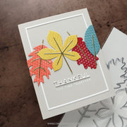 A handmade layered card featuring autumn leaves in yellow, red, and blue with gold foil accents, and the text 'THANKFUL FOR TIME TOGETHER'. A metal die is partially visible on the right against a textured brown background.