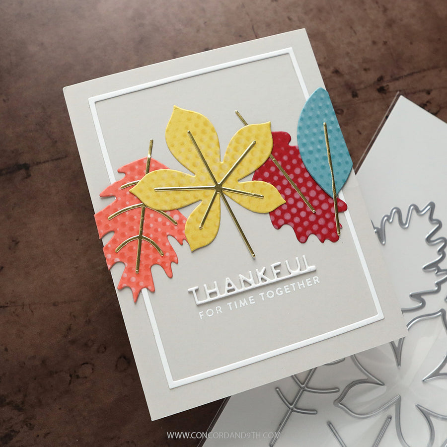 A handmade layered card featuring autumn leaves in yellow, red, and blue with gold foil accents, and the text 'THANKFUL FOR TIME TOGETHER'. A metal die is partially visible on the right against a textured brown background.