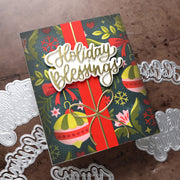 A handmade Christmas greeting card with a dark teal background, red ribbon, colorful ornaments, and a raised 'Holiday Blessings' die-cut element, styled with silver metal embosser dies on a brown textured surface.