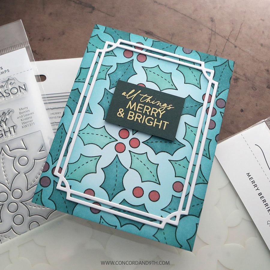 A handmade Christmas greeting card featuring a teal and white holly pattern with red berries and a central black label reading 'all things MERRY & BRIGHT' in gold foil, styled on a white surface with crafting tools partially visible.