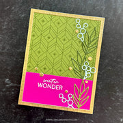 A handmade greeting card with a bright pink bottom section reading 'winter WONDER' and a green patterned top section, photographed on a dark textured surface.