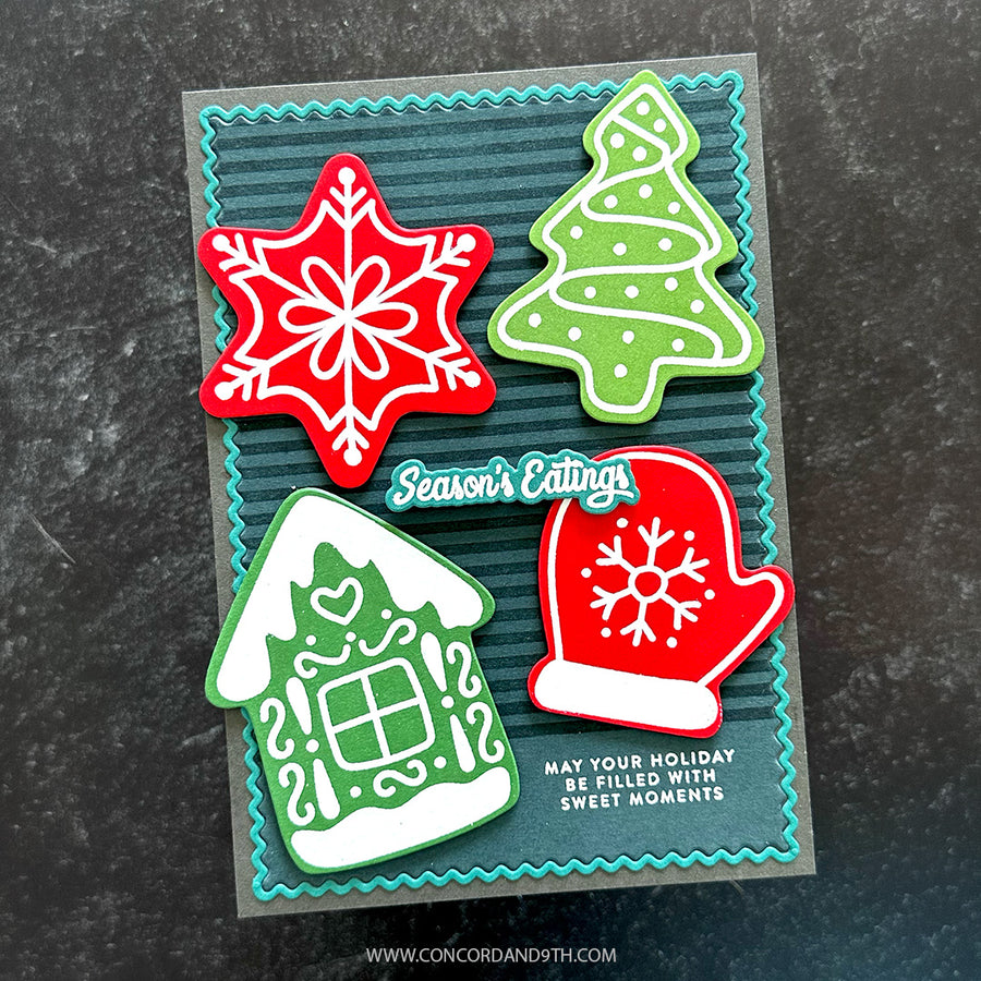 A handmade Christmas-themed card featuring four layered paper cutouts: a red snowflake, a green Christmas tree, a green house with white trim, and a red mitten with a white snowflake. The card has a dark teal striped background with a turquoise scalloped border and reads 'Season's Eatings' and 'MAY YOUR HOLIDAY BE FILLED WITH SWEET MOMENTS.
