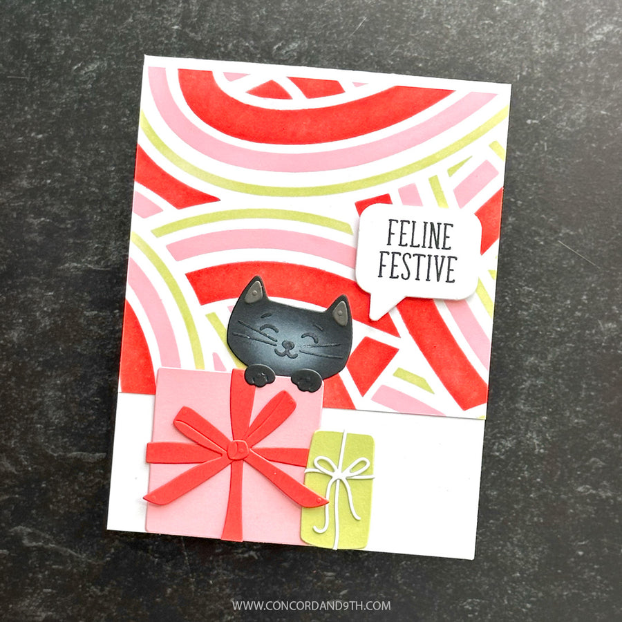 A handmade greeting card featuring a black cat illustration peeking over pink and green gift boxes with red and pink ribbon bows, set against a red, pink, and white wavy background. A speech bubble reads 'FELINE FESTIVE'.