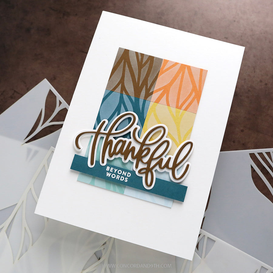 A handmade layered greeting card with a white cardstock base, featuring a colorful geometric pattern in teal, brown, orange, and yellow, with a die-cut script 'thankful' and a small 'BEYOND WORDS' tag. The card is displayed on a textured brown surface with other white cards partially visible underneath.
