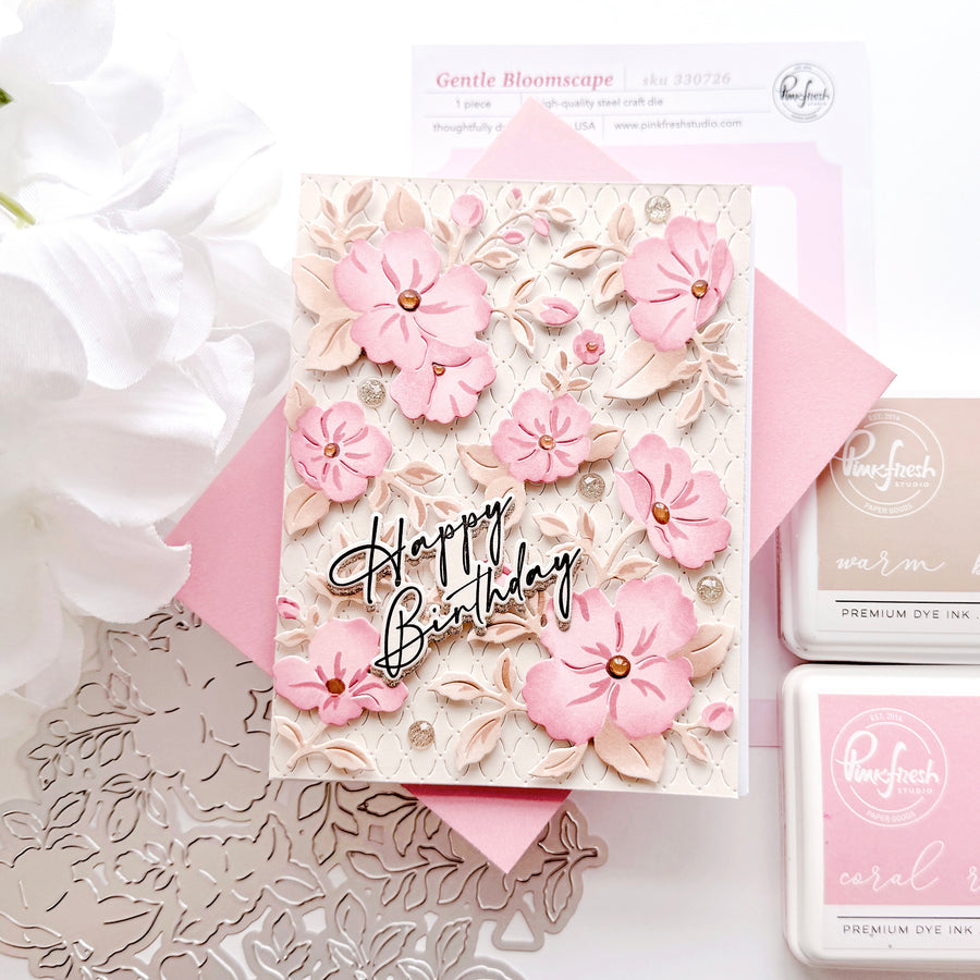 A handmade layered card with pink 3D flowers, beige leaf textures, and a black 'Happy Birthday' script overlay, styled with a pink envelope, dye ink pads, and a white flower on a white background.