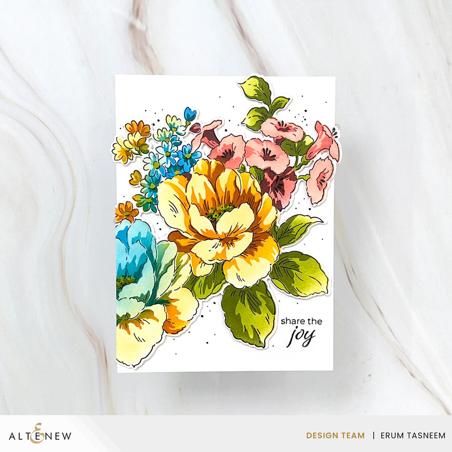 A floral handmade greeting card featuring a colorful watercolor-style bouquet with yellow, pink, blue, and green flowers on a white card, photographed on a light marble surface. The card has the phrase 'share the joy' printed in black script near the lower right.