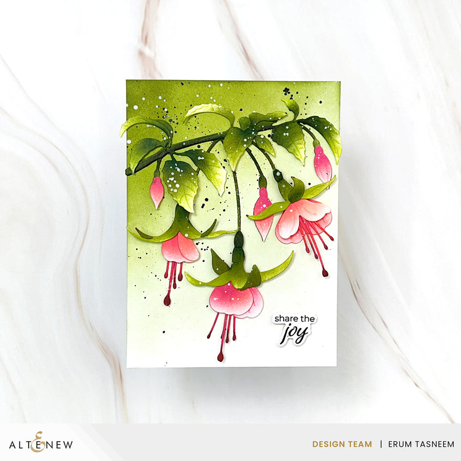 A handmade greeting card featuring a watercolor illustration of pink fuchsia flowers and green leaves on a white background with a green watercolor wash. The card has the text 'share the joy' printed on it.