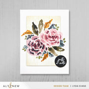 A watercolor floral handmade greeting card featuring pink and mauve flowers with green, brown, and orange leaves on a cream textured background, presented on a white card against a light gray wood backdrop. A black circular sticker reading 'just a note' is placed on the lower right of the card. Altenew One-Go: Solid Circular Sentiments Press Plate card ideas