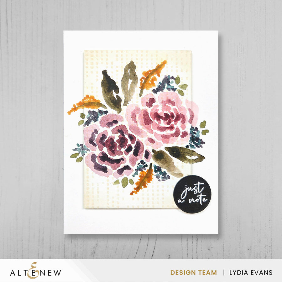 A watercolor floral handmade greeting card featuring pink and mauve flowers with green, brown, and orange leaves on a cream textured background, presented on a white card against a light gray wood backdrop. A black circular sticker reading 'just a note' is placed on the lower right of the card. Altenew One-Go: Solid Circular Sentiments Press Plate card ideas