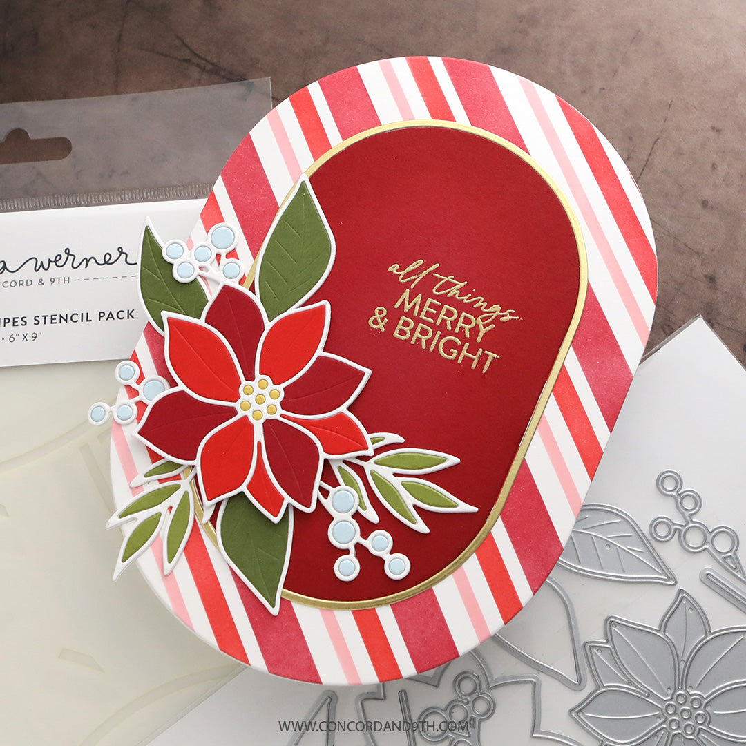 A handmade holiday greeting card featuring a red poinsettia with green leaves, red and white striped borders, and gold foil text reading 'all things MERRY & BRIGHT', shown on a tabletop with stencil packaging and metal stencils nearby.