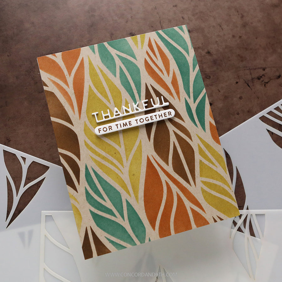 A handmade greeting card with a colorful leaf pattern in orange, teal, yellow, and brown, featuring a white die-cut sticker that reads 'THANKFUL FOR TIME TOGETHER'. The card is displayed on a white laser-cut tray over a textured brown background.