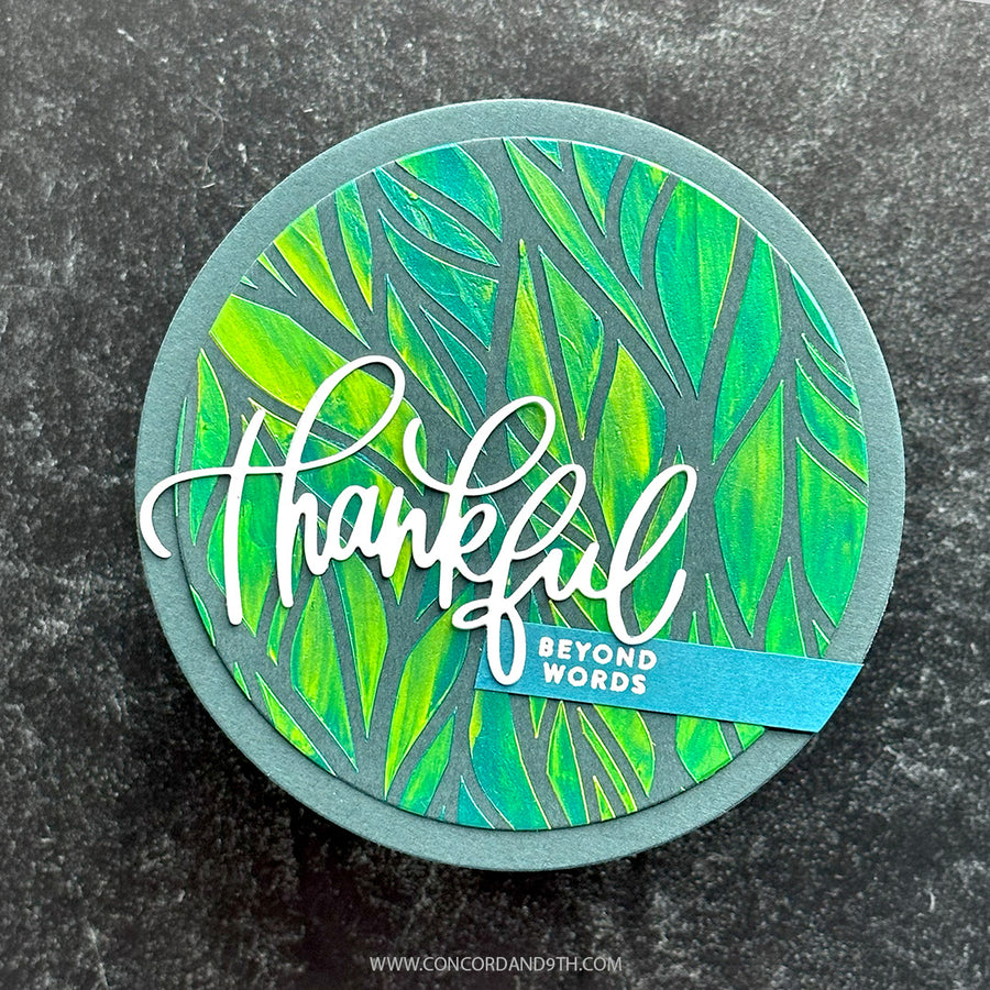 A round handmade greeting card or coaster featuring a green and yellow leaf pattern, a gray circular border, and the word 'thankful' in white script. A small blue banner reads 'BEYOND WORDS'.