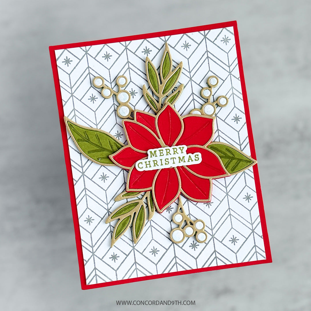 A handmade Christmas greeting card featuring a red poinsettia with green leaves and a 'Merry Christmas' banner, set against a white patterned background with a red border, photographed on a light gray marble surface.