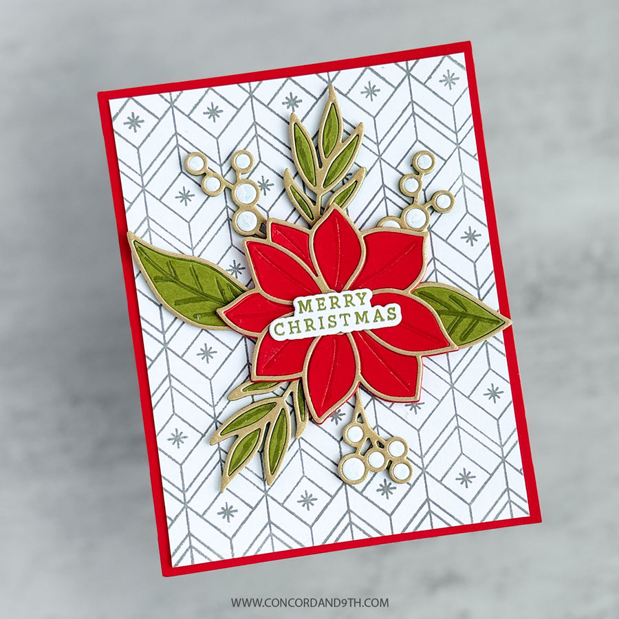 A handmade Christmas greeting card featuring a red poinsettia with green leaves and a 'Merry Christmas' banner, set against a white patterned background with a red border, photographed on a light gray marble surface.