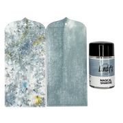 Two rectangular tags with rounded corners on a white background, alongside a small bottle labeled Lindi's Magical Shakers Moody Mist. The left tag shows a marbled icy blue and white pattern with small yellow accents, the right tag shows a mottled light blue texture, and the bottle contains the shaker paint.