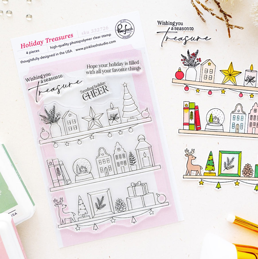 A clear stamp sheet labeled 'Holiday Treasures' by Pinkfresh Studio, shown alongside a printed sample of the holiday-themed stamp designs on a white background with decorative props.