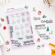A sheet of clear stamp designs called Tiny Tidings by Pinkfresh Studio featuring Christmas-themed illustrations and phrases like 'Peace, Love, & Joy' and 'Celebrate the Season,' shown on a light background with small decorative props.
