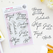 A flat-lay of Pinkfresh Studio's Simply Said 8-piece clear photopolymer stamp set on a white background, alongside matching black script letter stickers spelling birthday and greeting phrases.