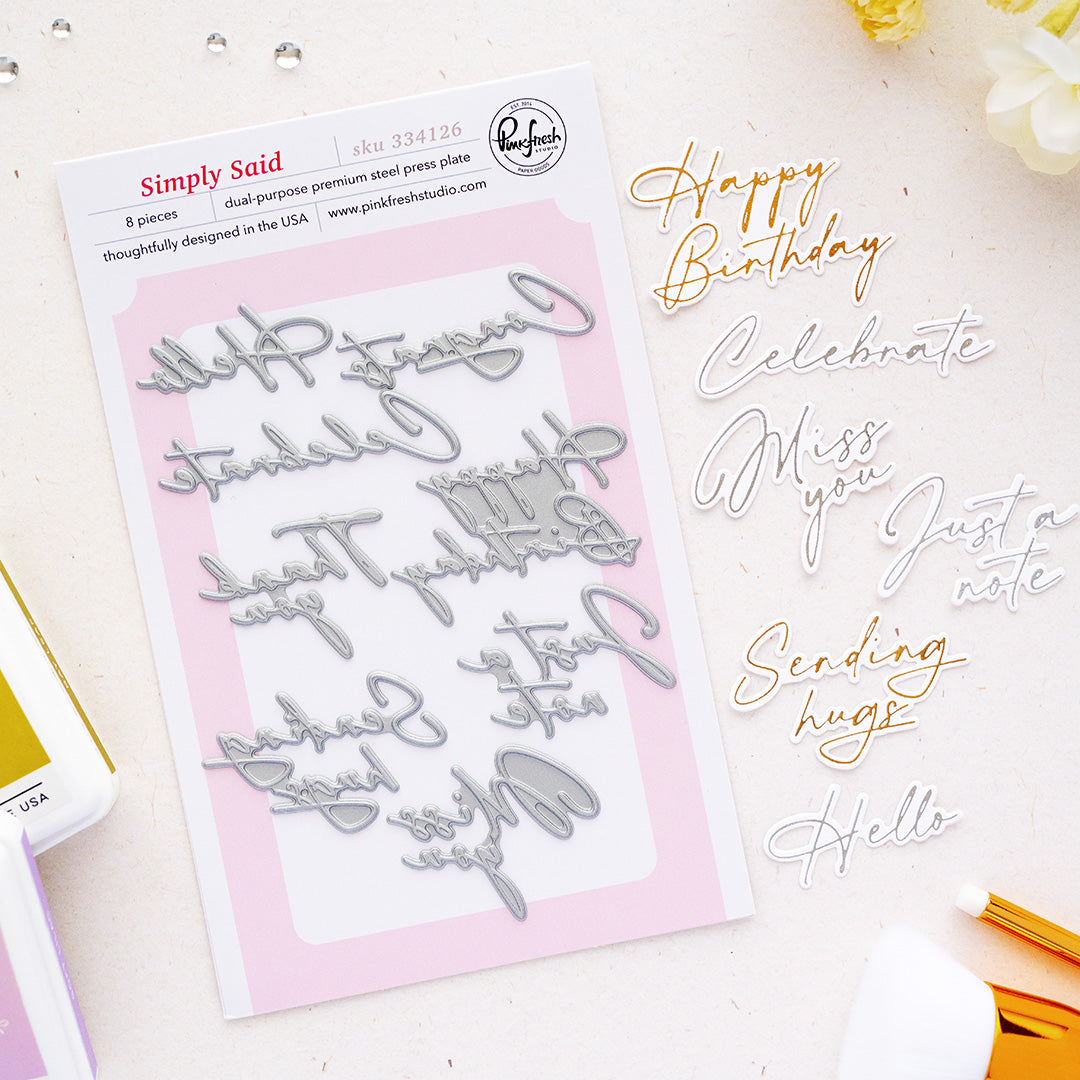 Simply Said Press Plates by Pinkfresh Studio on a white card, styled on a light beige surface with gold and silver metallic lettering examples and craft tools.