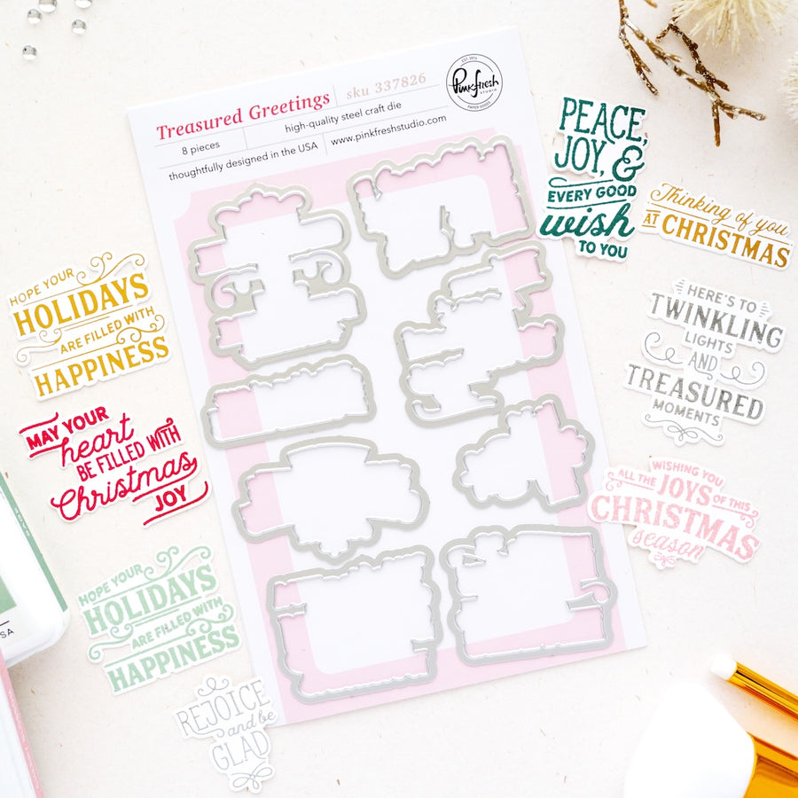 A flat-lay of a metal die-cut craft sheet from Pinkfresh Studio titled 'Treasured Greetings'. The sheet contains multiple Christmas-themed die-cut templates in silver, set against a light pink and white patterned backing.