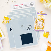 A styled flat-lay of a Pinkfresh Studio stencils set called 'Steeped in Comfort' black inked stamp impressions, surrounded by decorative stickers and branding cards on a white background.