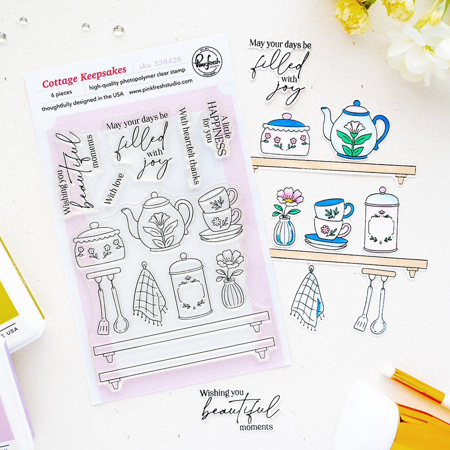 A sheet of clear stamp designs with floral tea-themed illustrations and phrases, displayed on a white surface alongside an example stamped design. The packaging reads 'Cottage Keepsakes' and '8-piece clear stamp' by Pinkfresh Studio.