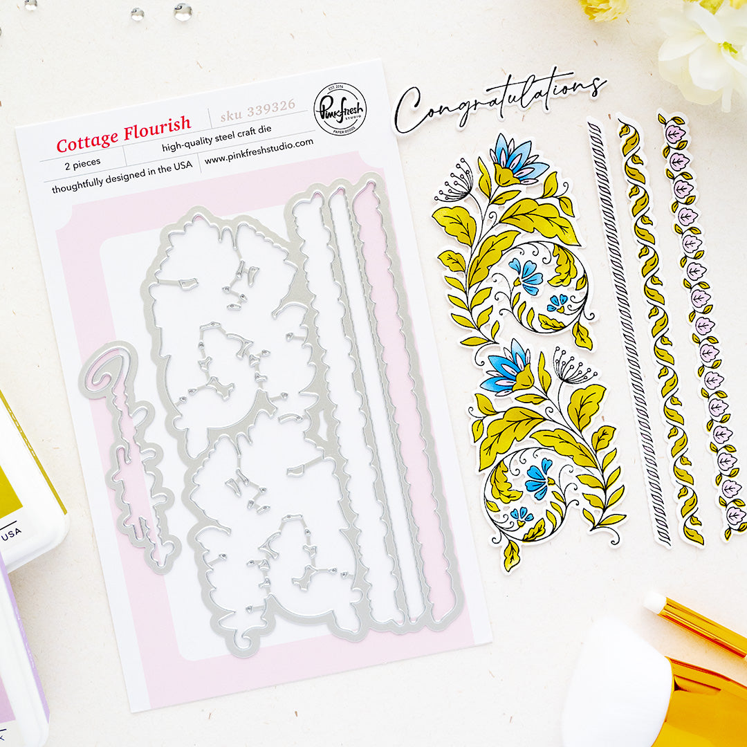 A flat-lay product shot of a steel cutting dies by Pinkfresh Studio called Cottage Flourish, showing the metal cutting dies on a sheet next to sample stamped floral designs and decorative borders on a white background.