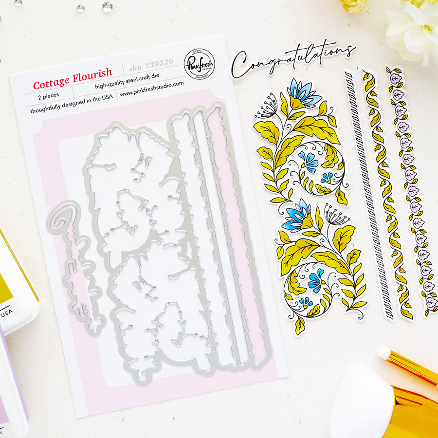 A flat-lay product shot of a steel cutting dies by Pinkfresh Studio called Cottage Flourish, showing the metal cutting dies on a sheet next to sample stamped floral designs and decorative borders on a white background.