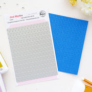 A flat-lay product photo of a pink and white paper insert for an oval mesh craft die, next to a blue textured sheet showing the die's imprint. The insert features the brand logo for 'Pinkfresh Studio' and the product name 'Oval Rhythm'.