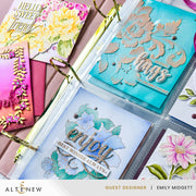 A close-up of a clear plastic ring binder holding handmade greeting cards with floral and decorative designs. Visible cards include turquoise, white, pink, and yellow floral layouts with metallic foil details.
