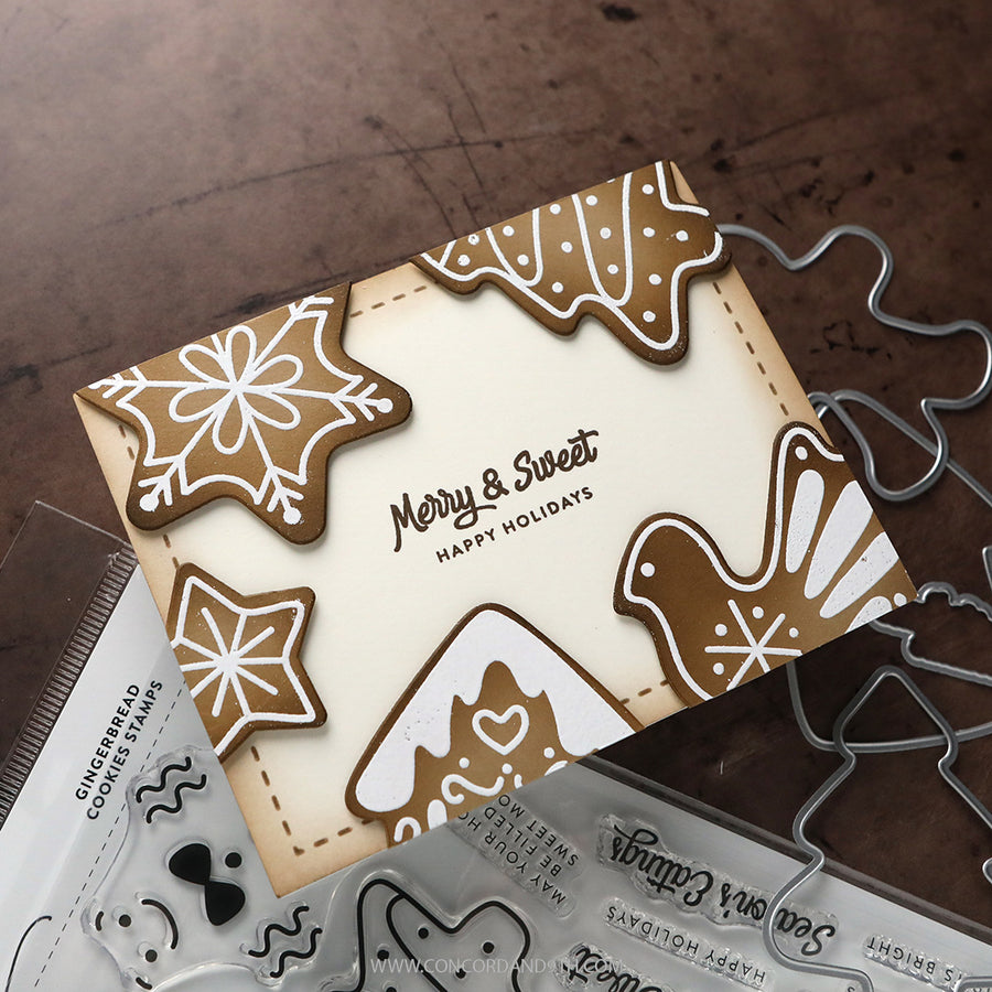 A handmade Christmas card with gingerbread cookie illustrations and the text 'Merry & Sweet Happy Holidays,' shown on a wooden surface with clear stamp sheets and metal die cutters nearby.