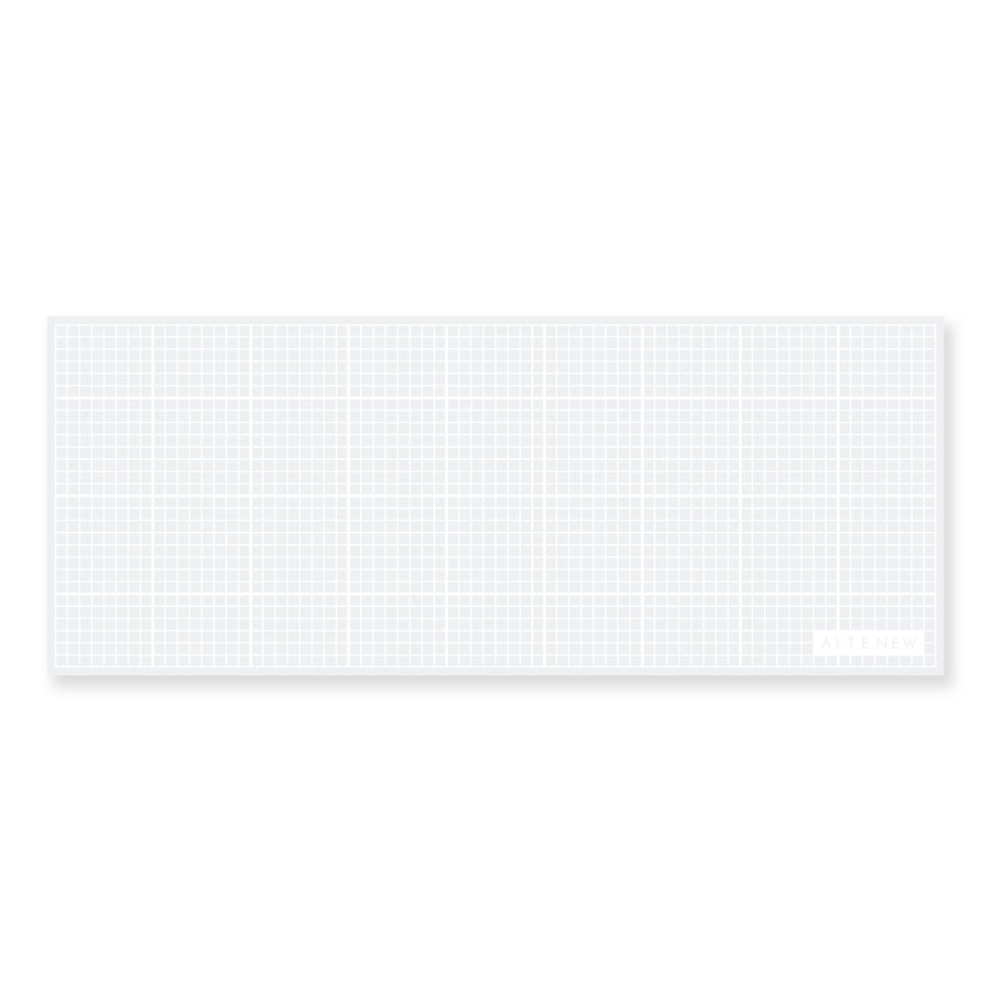 A white rectangular mat with a fine gray grid pattern and a small white label in the bottom right corner, shown on a plain white background. Altenew The Original Mini Sticky Mat: 9" x 3.5" (Classic Grid)