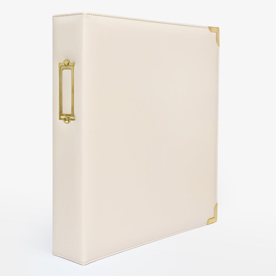 An ivory-colored faux leather ring binder with gold-tone metal accents, including a decorative side handle and corner protectors, shown on a clean white background. 