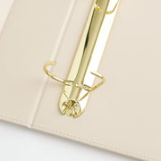 Close-up of an ivory-colored ring binder with a shiny gold metal ring frame and binding hardware. 