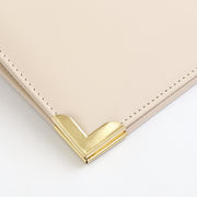 Close-up of an ivory leather corner with a polished gold-tone metal chevron accent and matching stitching on a white background. 