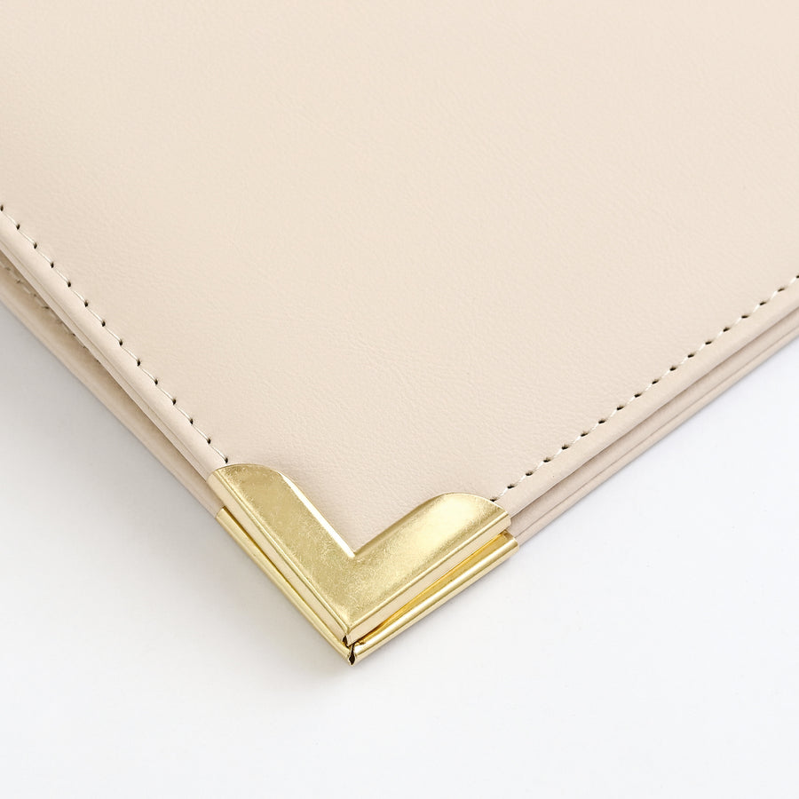 Close-up of an ivory leather corner with a polished gold-tone metal chevron accent and matching stitching on a white background. 