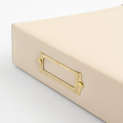 A close-up of an ivory-colored leather or faux-leather storage box with a gold metal label holder handle, set against a clean white background. 
