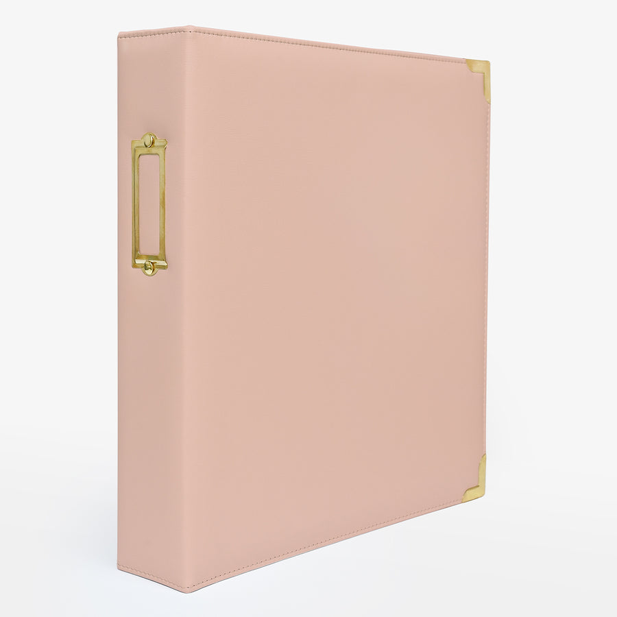 A rouge faux leather ring binder with gold-tone metal corner protectors and a vertical ring slot on the spine, shown on a clean white background. 