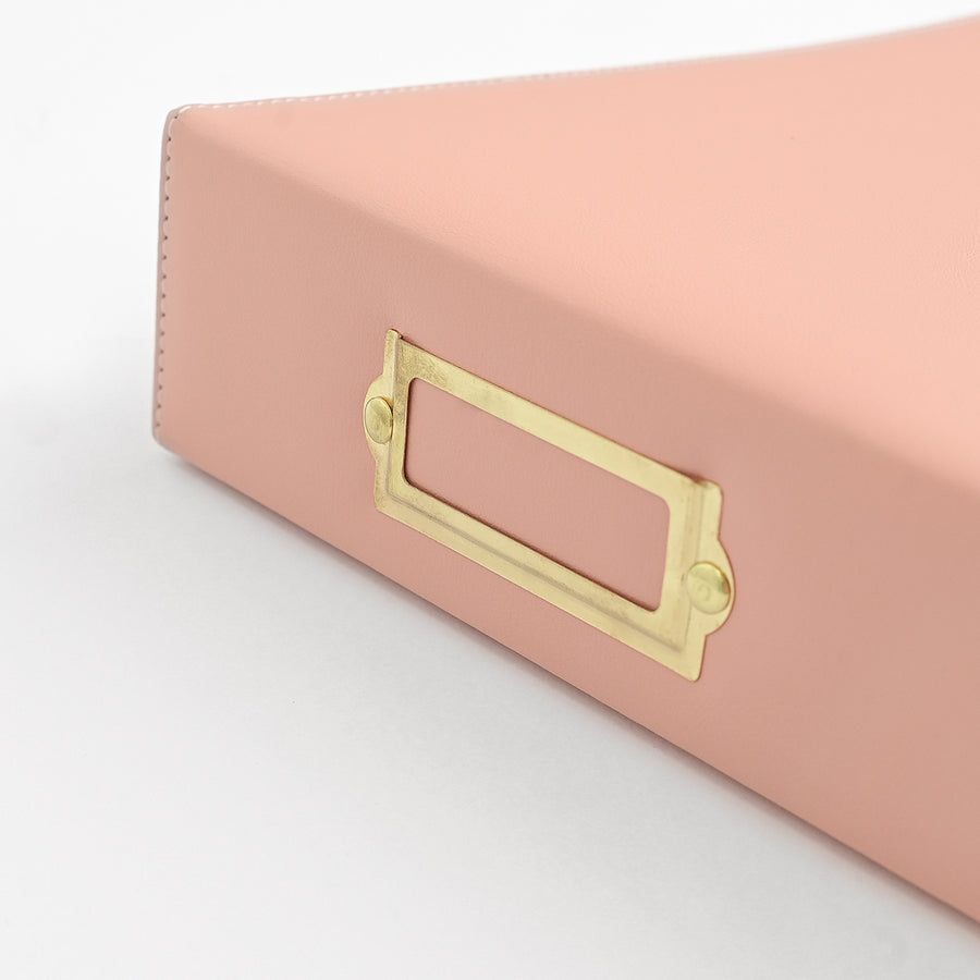 A close-up of a rouge leather document folder or organizer with a gold metal label holder on a white background. 