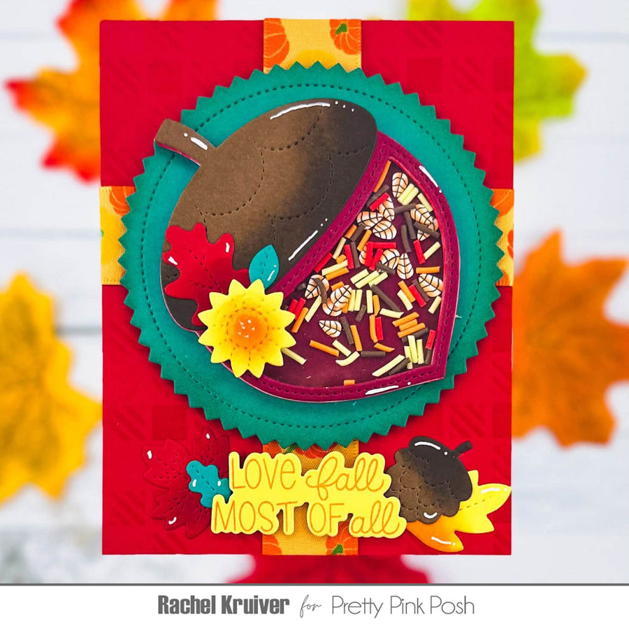 A handmade autumn-themed layered card featuring a die-cut leaf design with a brown acorn, colorful confetti-filled window, yellow flower, and the phrase 'Love fall most of all' on a red background with blurred fall leaves.