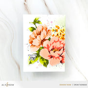 A handmade greeting card featuring watercolor-style flowers in peach, pink, and orange with green leaves, plus the phrase 'share the joy' in black script. The card is photographed on a light marble surface, with ALTENEW branding and designer credit at the bottom.