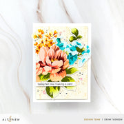 A handmade layered card featuring a large peach flower, blue flowers, yellow blossoms, and green leaves on a cream background with a small banner reading 'today felt like making a card'. The card is photographed on a light marble surface, with Altenew and Erum Tasneem branding visible at the bottom.