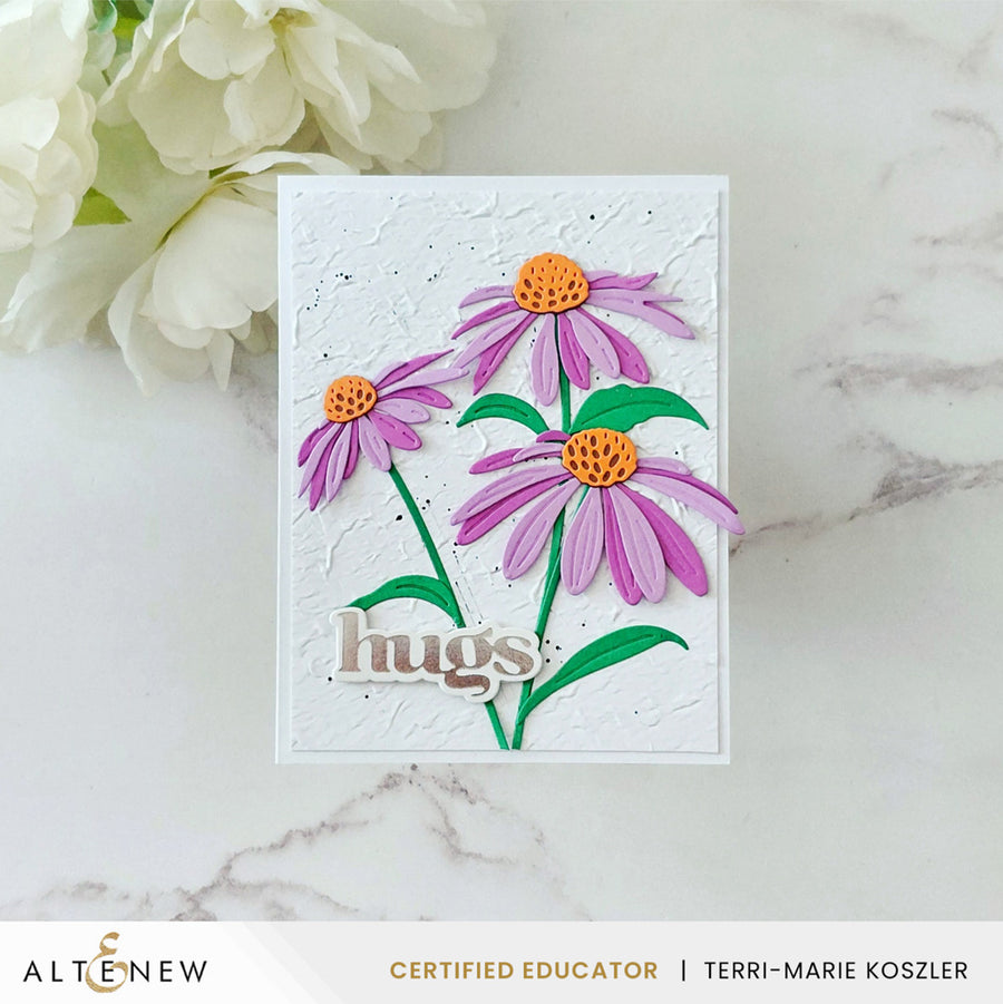 A handmade greeting card featuring three purple coneflowers with orange centers and green stems on a white textured background, with the word 'hugs' in metallic script. The card is displayed on a light marble surface next to white flowers, with an ALTENEW banner at the bottom. Altenew Craft-A-Flower: Coneflower Layering Die Set card ideas