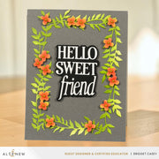 A handmade greeting card with a dark gray background, featuring a raised black and white 'HELLO SWEET friend' text element surrounded by layered green leaves and orange flowers, displayed on a wooden surface.