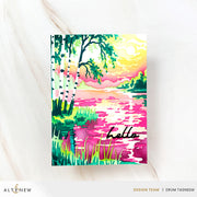 A colorful watercolor-style handmade greeting card featuring a lakeside landscape with green trees, pink and yellow sky, and the word 'hello' in black script near the bottom. The print is photographed on a light marble-like surface with branding text at the bottom of the image. Altenew Craft Your Life Project Kit: Painterly Perfection card ideas