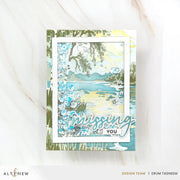 A handmade layered card featuring a watercolor-style lake landscape with blue and green tones, floral embellishments, and the words 'missing YOU' in script and block lettering, displayed on a light marble surface. Altenew Craft Your Life Project Kit: Painterly Perfection card ideas