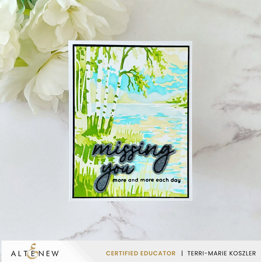 A handmade greeting card with a watercolor-style landscape of green trees and blue sky, featuring the text 'missing you more and more each day' in black script. The card is displayed on a white marble surface next to white flowers, with an Altenew Certified Educator banner at the bottom. Altenew Craft Your Life Project Kit: Painterly Perfection card ideas
